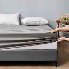 Housse de matelas grise dont le bord est étiré à la main au pied d’un lit avec deux oreillers blancs.